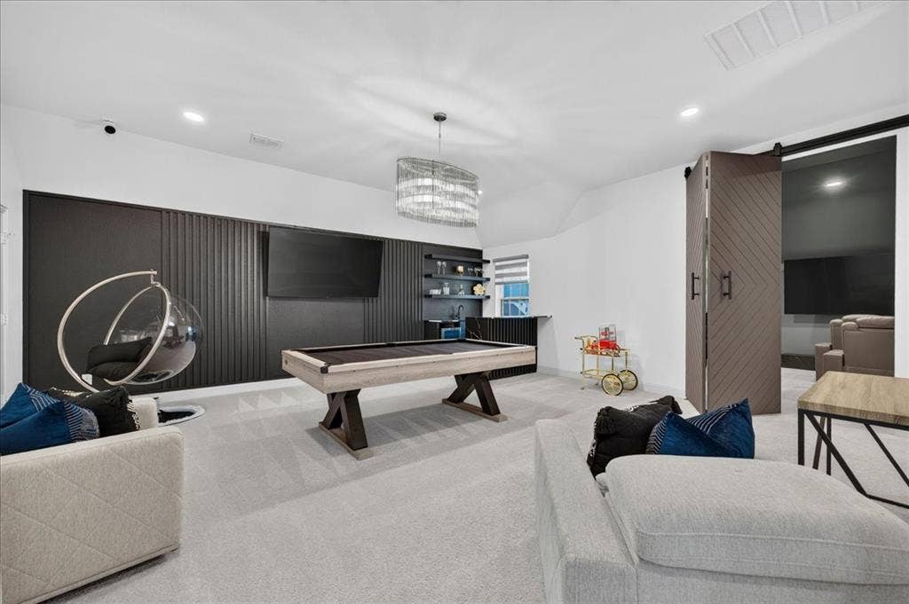 Spacious recreational room featuring light-toned carpeting and a contemporary chandelier