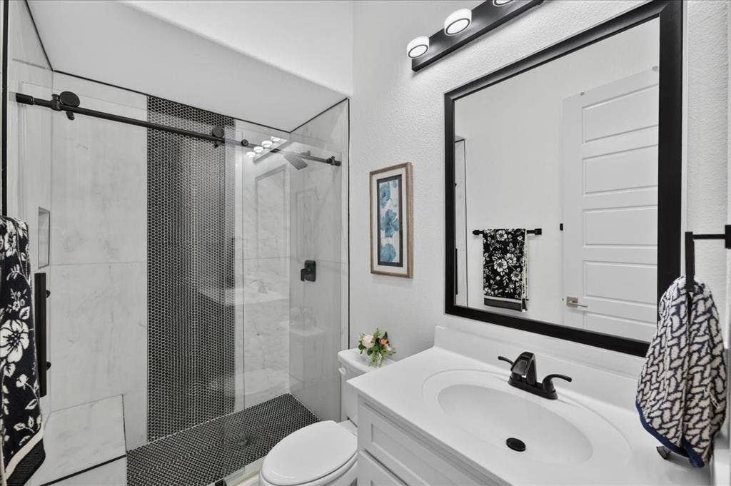 Modern bathroom featuring a glass-enclosed shower with black penny tile accent, a white vanity with integrated sink, and a framed mirror with black trim