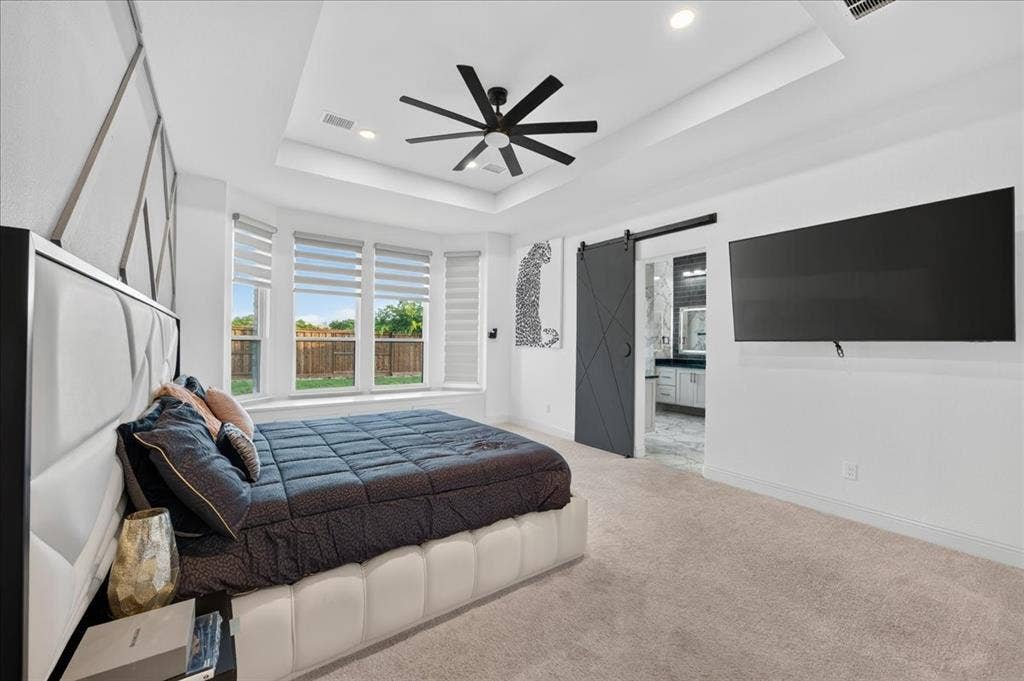 Spacious bedroom featuring a tray ceiling with recessed lighting, a modern black ceiling fan, and carpeted flooring
