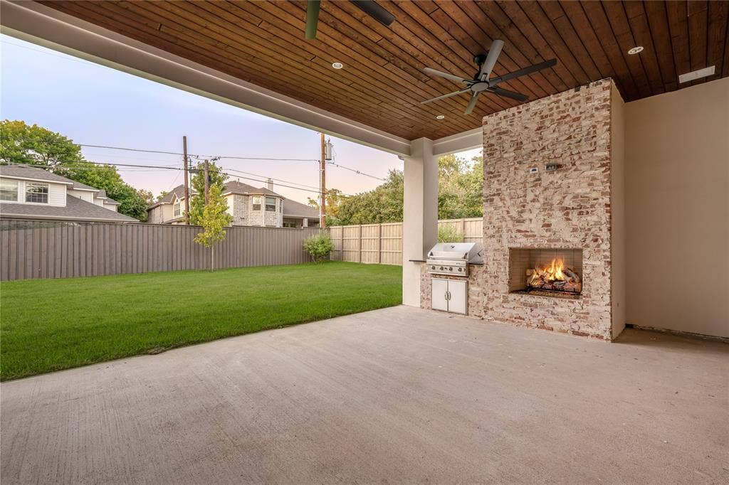 Expansive covered patio with a wood-finish plank ceiling, two ceiling fans, and a brick fireplace