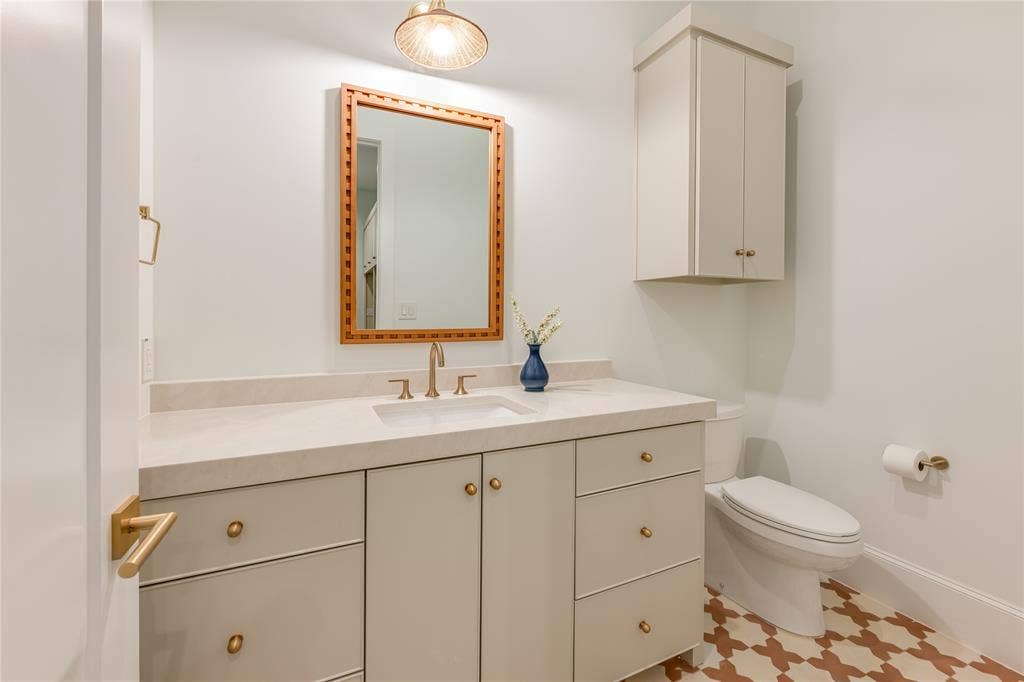 Vanity with integrated sink, rectangular mirror with a decorative frame, wall-mounted upper cabinetry, and patterned floor tiling
