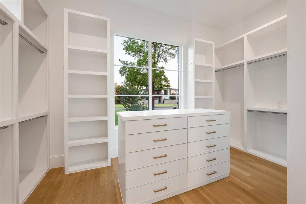 Built-in white cabinetry, central dresser island with brass hardware, wood-finish flooring, and a large window with grid pattern