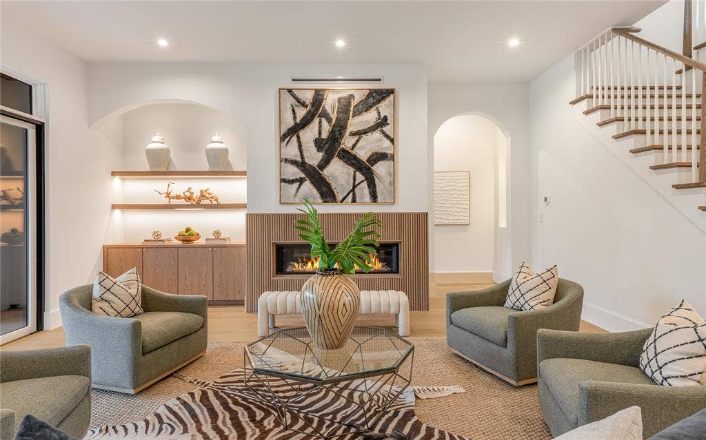 Built-in cabinetry with illuminated shelving, a linear fireplace with wood-finish surround, hardwood flooring, and a hardwood staircase with white risers