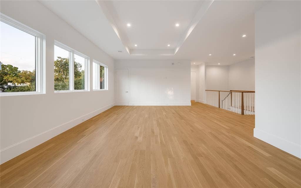 Expansive room featuring light wood-finish flooring, multiple windows, a tray ceiling with recessed lighting, and a white baluster railing