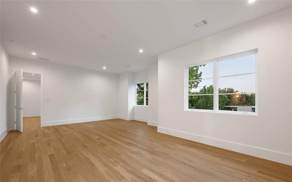 Spacious room with wood-finish flooring, recessed lighting, white walls, and multiple windows