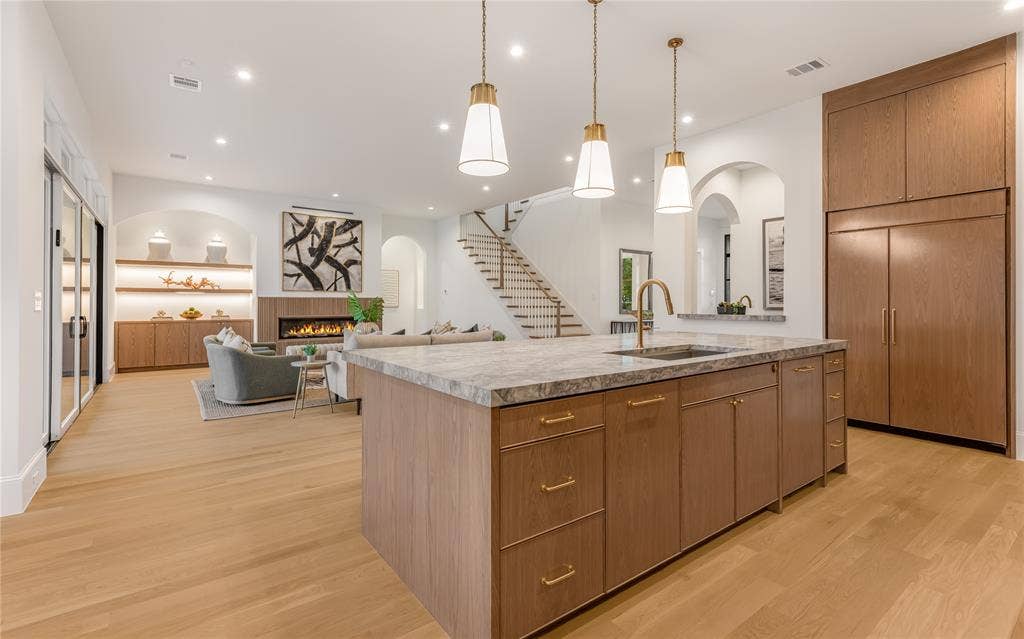 Open-concept living area with wood-finish flooring, a kitchen island featuring a sink, and integrated wood-finish cabinetry