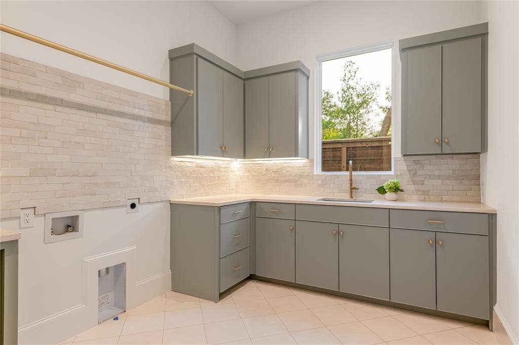 Built-in cabinetry, under-cabinet lighting, stainless steel sink with a gold-tone faucet, tile backsplash, and light-toned tile flooring