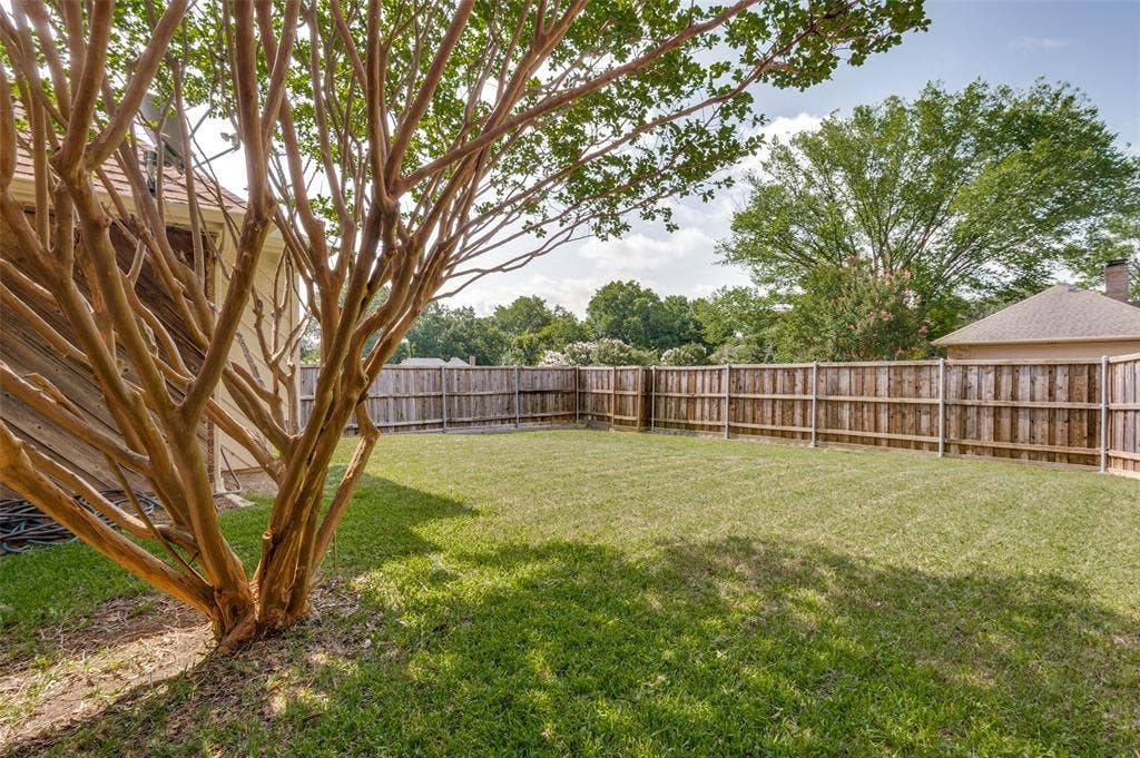 Generous backyard featuring a manicured lawn, full privacy fencing, and mature trees