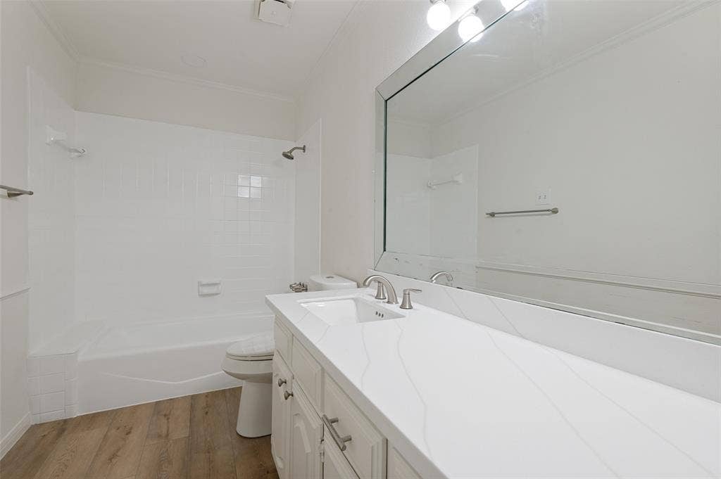 Bathroom featuring a single vanity with a white countertop and undermount sink, wood-finish flooring, a combination tub and shower with white subway tile surround, and a large wall-mounted mirror