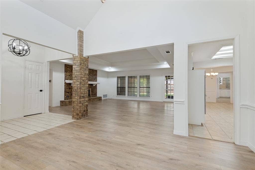 Expansive open-concept living area featuring wood-finish flooring, a vaulted ceiling, and a brick fireplace