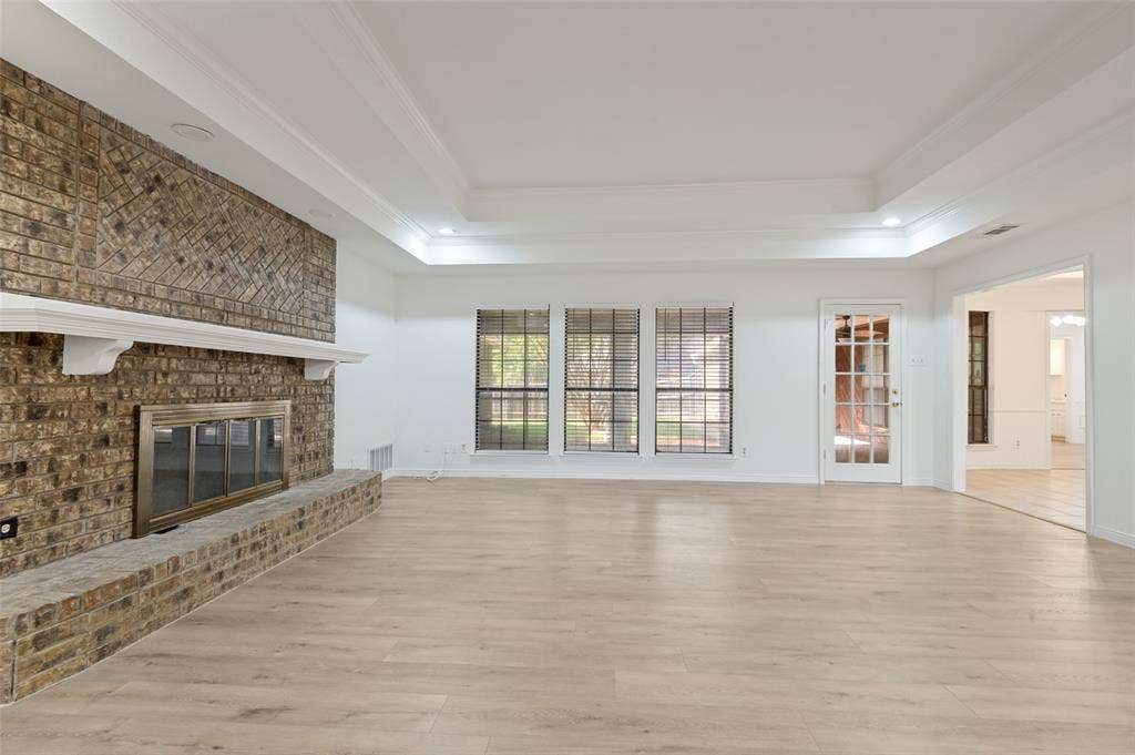 Spacious living area featuring a brick fireplace with a white mantel, wood-finish flooring, and a tray ceiling with recessed lighting