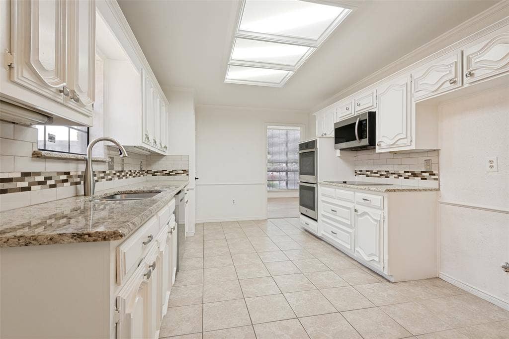 Kitchen featuring white cabinetry, granite countertops, a stainless steel sink with a gooseneck faucet, a subway tile backsplash with decorative accents, and tiled flooring