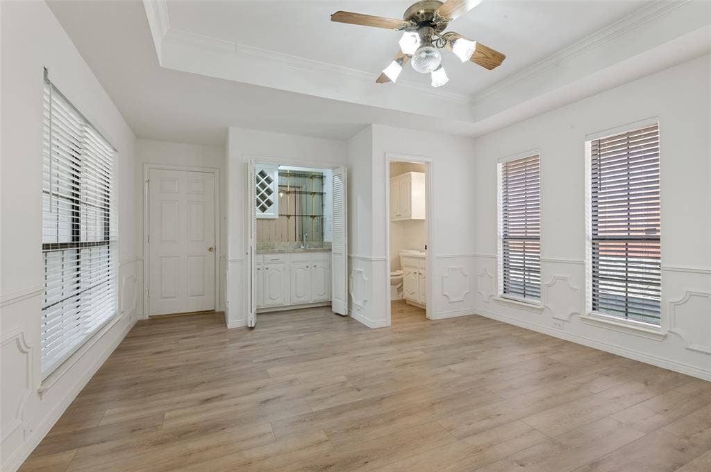 Spacious room featuring wood-finish flooring, a tray ceiling with a fan light fixture, and decorative wainscoting