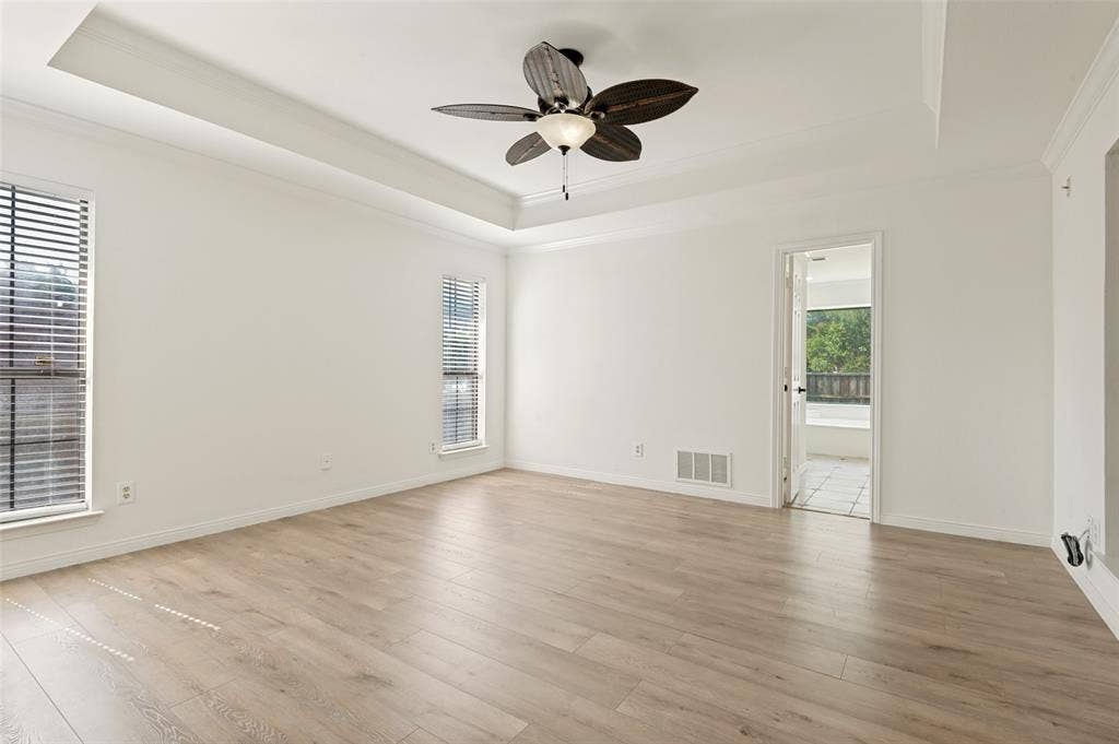Expansive room featuring wood-finish flooring, a tray ceiling with a ceiling fan, and two windows with blinds