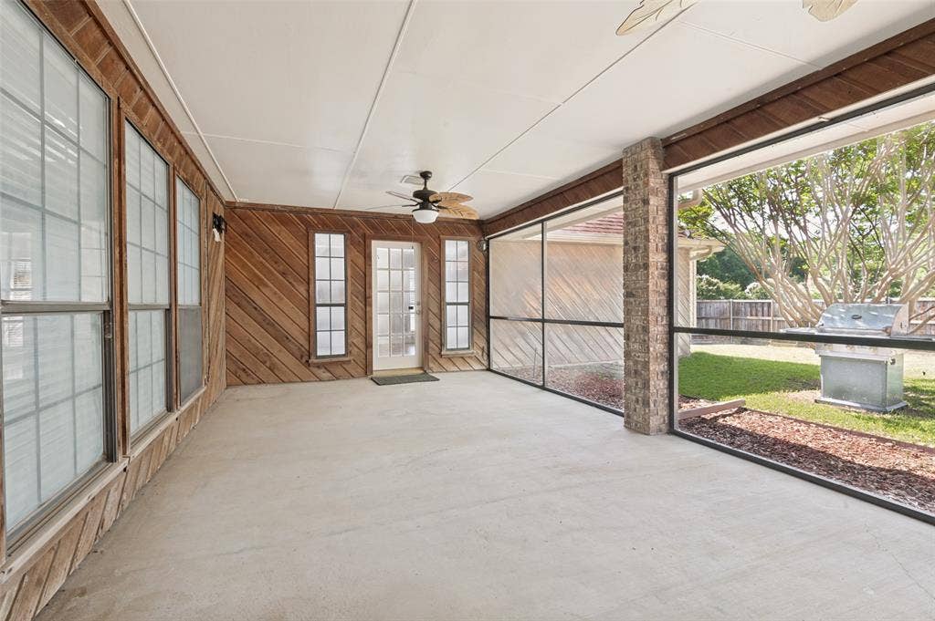 Expansive screened patio featuring a concrete floor, wood-paneled walls, and two ceiling fans with integrated lighting