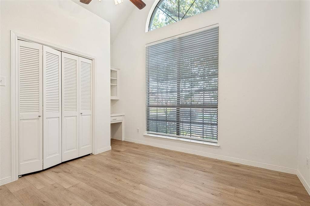 Spacious room featuring vaulted ceilings, wood-finish flooring, and a large window with an arched transom