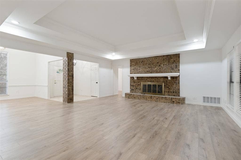Spacious interior featuring wood-finish flooring, a brick fireplace with a white mantel, and tray ceilings