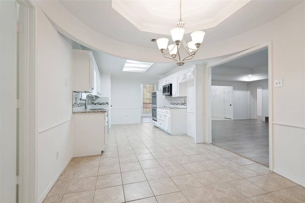 Spacious kitchen featuring white cabinetry, light-toned tile flooring, and a decorative backsplash