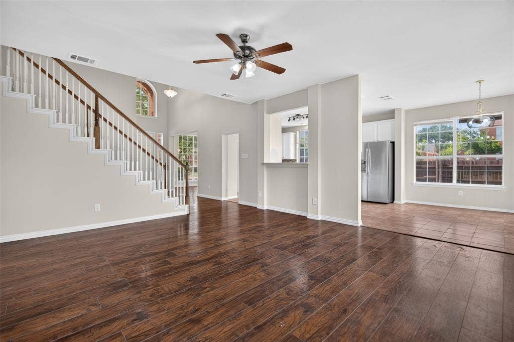 7112 Chandler Drive, Plano, TX 75024 Spacious living area featuring wood-finish flooring, a contemporary ceiling fan, and a prominent staircase with white risers and a dark wood handrail