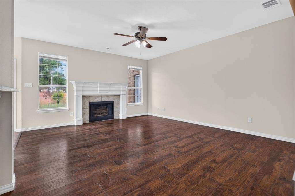 7112 Chandler Drive, Plano, TX 75024 Spacious room featuring wood-finish flooring, a decorative fireplace with a tile surround and substantial mantel, multiple windows, and a ceiling fan