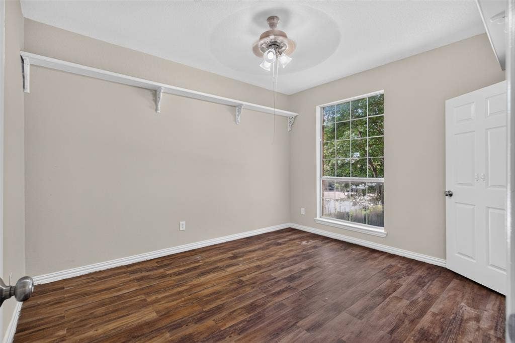 7112 Chandler Drive, Plano, TX 75024 Room featuring wood-finish flooring, a large window, a ceiling fan with light fixture, and a built-in shelving system