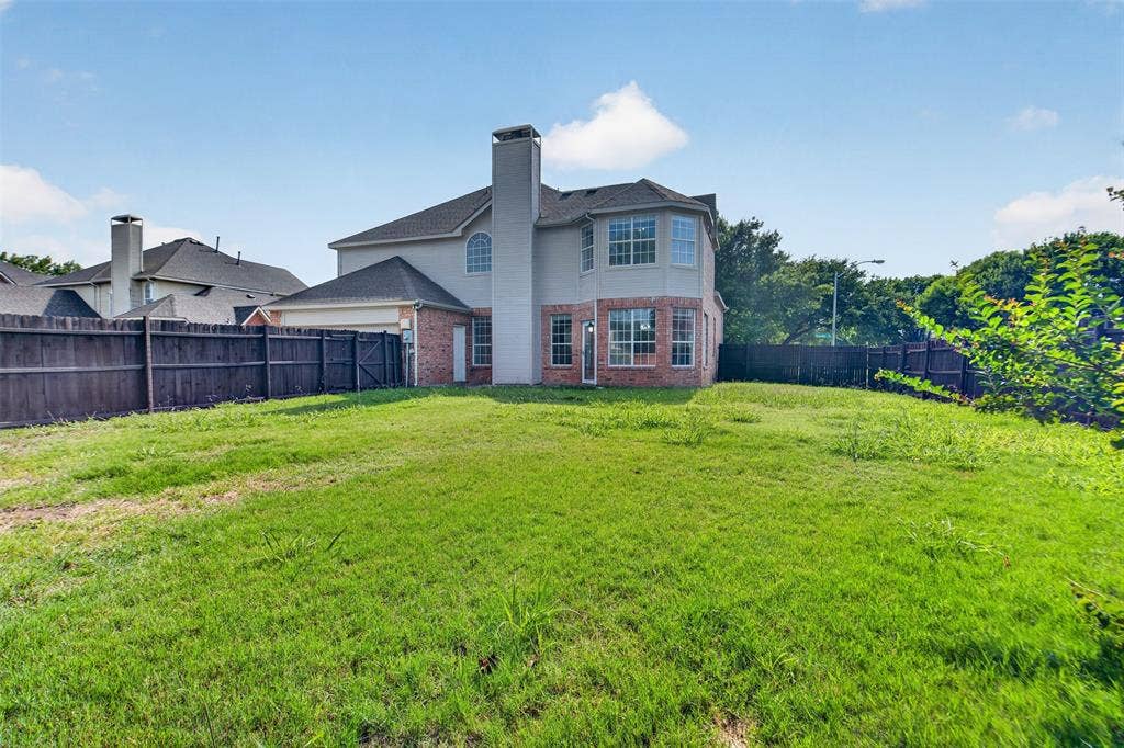 7112 Chandler Drive, Plano, TX 75024 Spacious backyard with a partial brick and siding exterior, featuring multiple windows, a prominent chimney, and a privacy fence