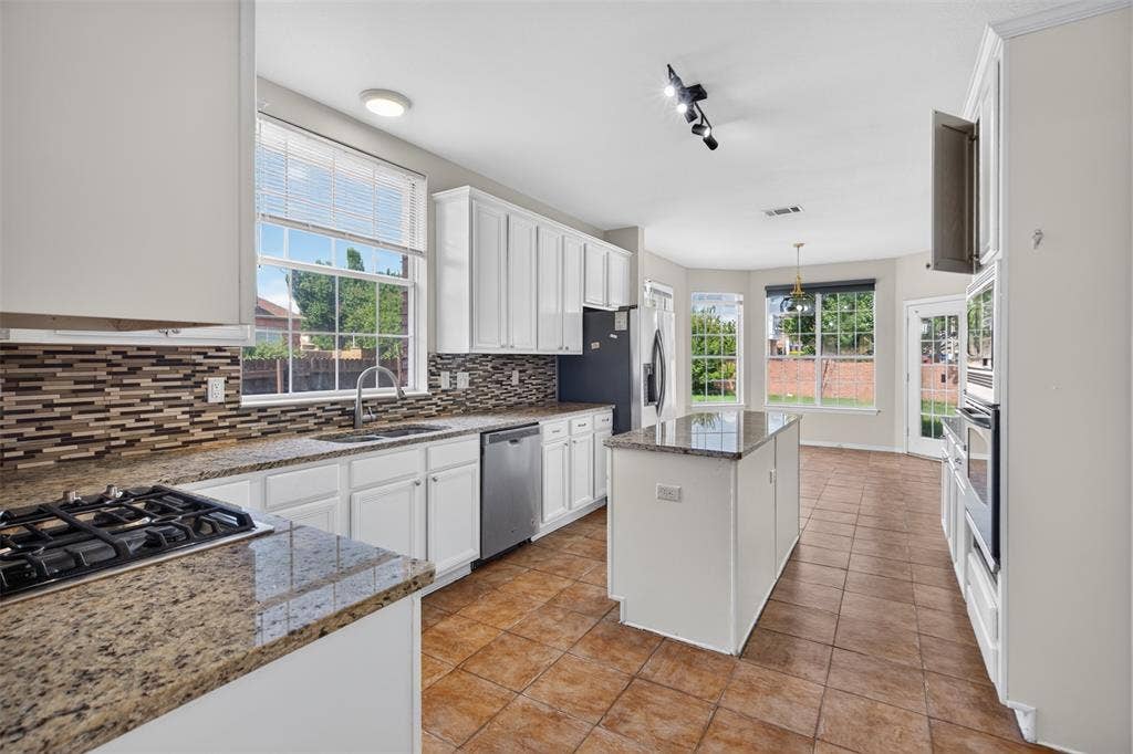 7112 Chandler Drive, Plano, TX 75024 Kitchen featuring white cabinetry, granite countertops, a gas cooktop, a mosaic tile backsplash, and a central island