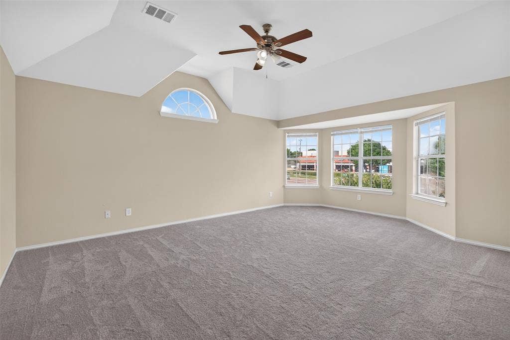 7112 Chandler Drive, Plano, TX 75024 Spacious room featuring vaulted ceilings, a ceiling fan, bay windows, an arched transom window, and neutral-toned carpeting
