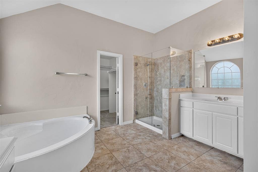 7112 Chandler Drive, Plano, TX 75024 Bathroom featuring a corner soaking tub, a glass-enclosed shower with tiled walls, a single vanity with storage, a large mirror, and tiled flooring