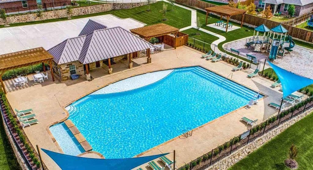 1214 Cedar Branch Drive, Wylie, TX 75098 Resort-style pool area featuring a large swimming pool with concrete decking, an adjacent shaded pergola, and a stone-clad amenity building