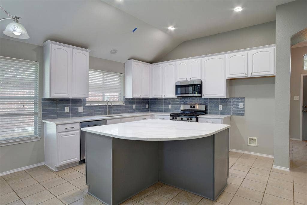 1214 Cedar Branch Drive, Wylie, TX 75098 Kitchen featuring a curved central island with light-toned countertops, white cabinetry, a blue tile backsplash, stainless steel appliances, and tile flooring