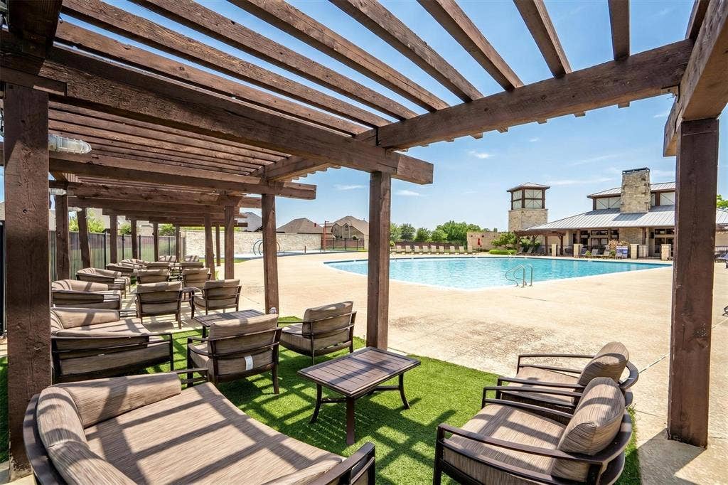 Expansive outdoor pool area featuring a large swimming pool, a substantial clubhouse with stone accents, and an extensive pergola structure