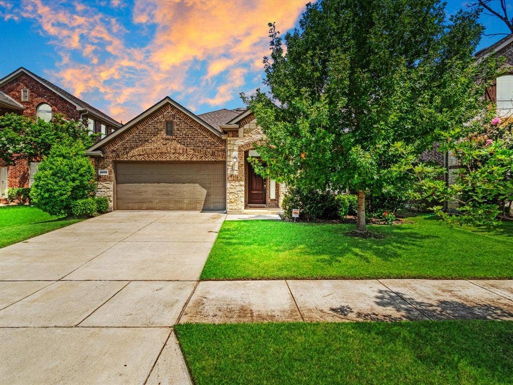 Brick and stone facade residence featuring an attached garage, a concrete driveway, and a well-maintained lawn with established trees