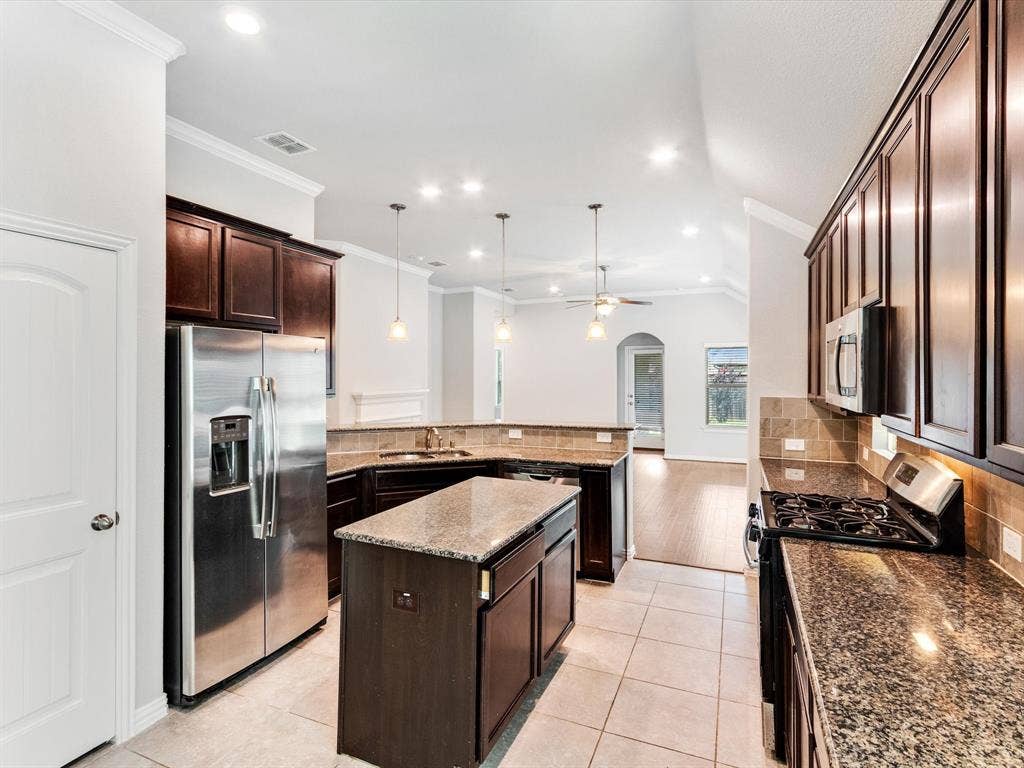 Kitchen featuring stone-finish countertops, wood-finish cabinetry, stainless steel appliances, a center island, and tile flooring