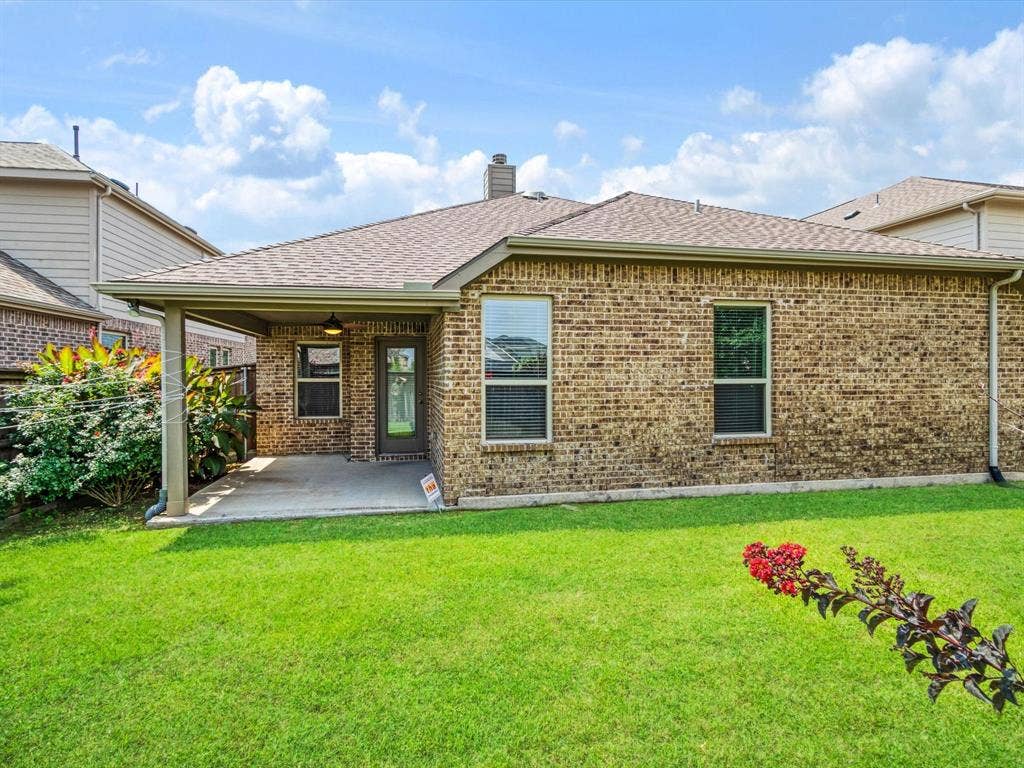 Expansive backyard featuring a covered patio with concrete flooring, a brick exterior, a shingle roof, and established landscaping