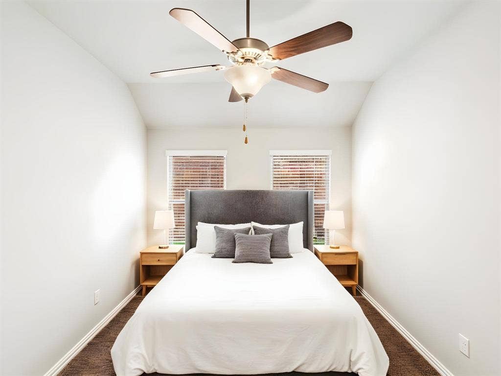 Vaulted ceiling bedroom featuring a ceiling fan with light fixture, two windows with blinds, and brown carpet flooring
