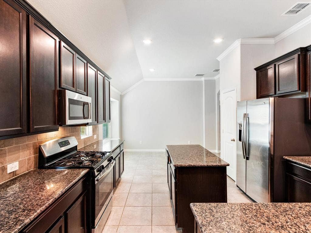 Kitchen featuring dark wood cabinetry, stainless steel appliances, granite countertops, a tiled backsplash, and recessed lighting