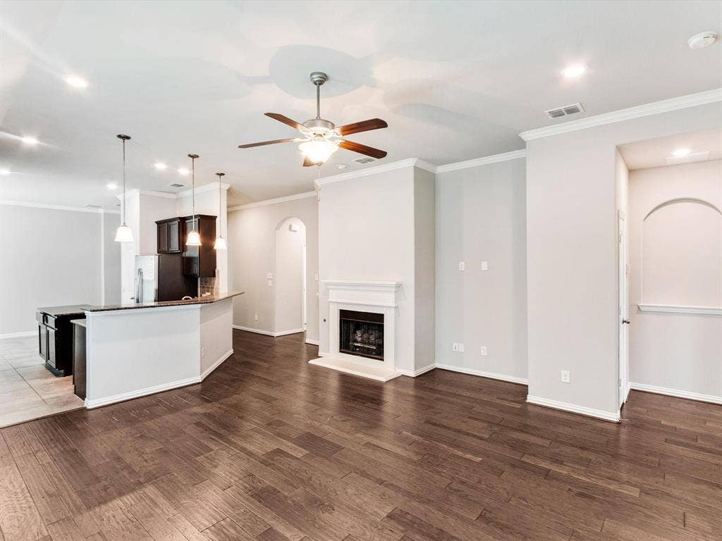 Open-concept living space with dark wood-finish flooring, a central fireplace, and a ceiling fan