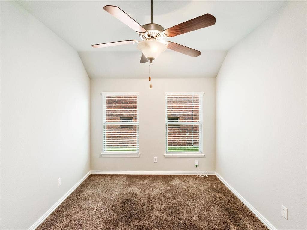 Room featuring a vaulted ceiling with a ceiling fan, two windows with blinds, brown carpet, and white baseboards