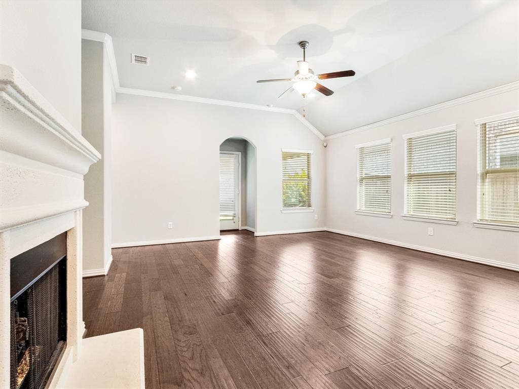 Spacious interior featuring dark wood-finish flooring, a white mantel fireplace, and vaulted ceilings with a ceiling fan