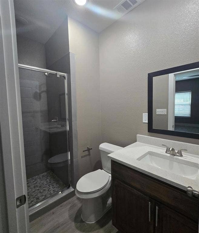 3513 Tomahawk Drive, Granbury, TX 76048 Contemporary bathroom featuring a glass-enclosed shower with pebble-style floor, a dark wood-finish vanity with a white countertop and integrated sink, brushed nickel fixtures, and wood-finish flooring