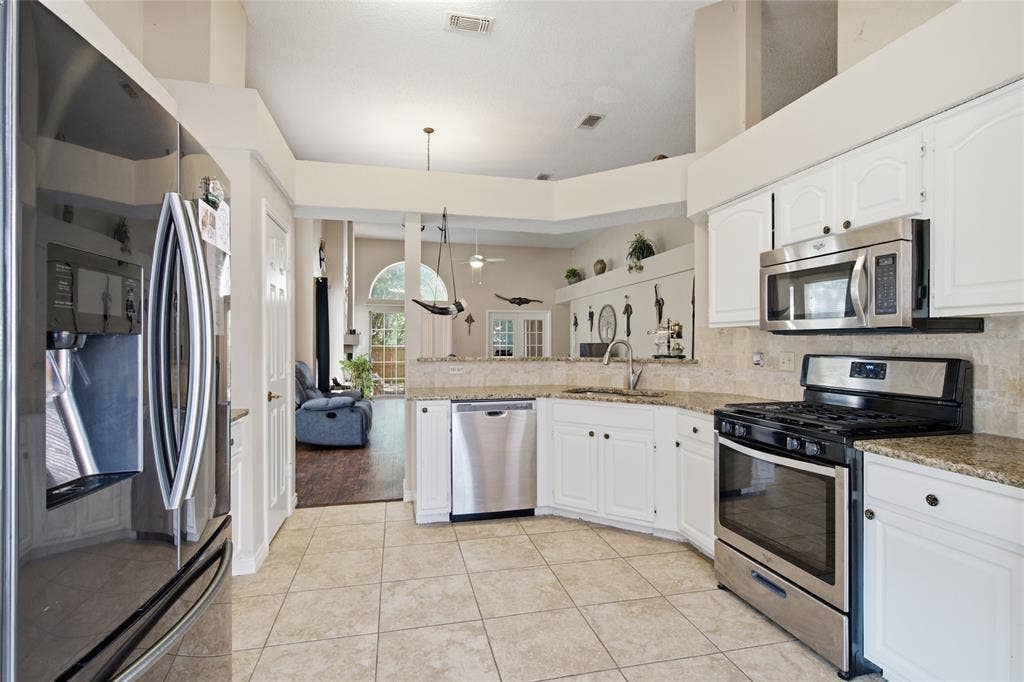1106 Cain Court, Cedar Hill, TX 75104 Contemporary kitchen featuring white cabinetry, granite countertops, and stainless steel appliances including a built-in microwave, gas range, and dishwasher