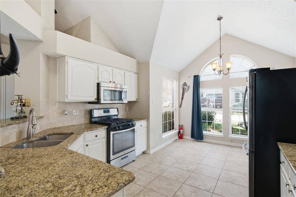 1106 Cain Court, Cedar Hill, TX 75104 Kitchen and dining area featuring vaulted ceilings, light-colored tile flooring, granite-finish countertops, white cabinetry, and an integrated stainless steel microwave with a gas range