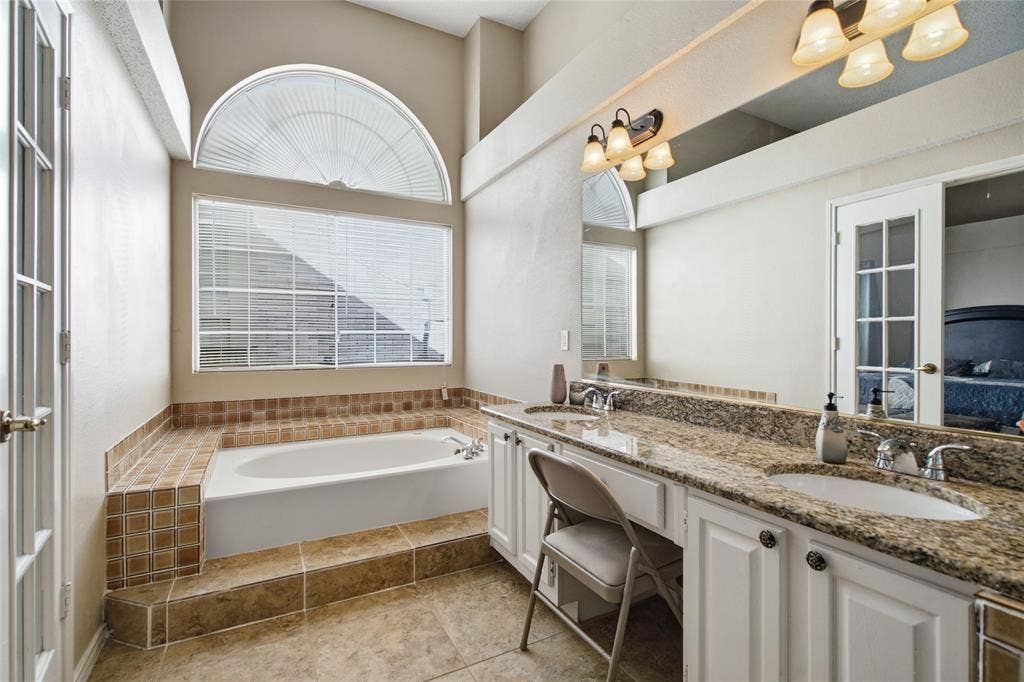 1106 Cain Court, Cedar Hill, TX 75104 Spacious bathroom featuring a built-in soaking tub with tiled surround, an arched transom window, and a dual vanity with granite-finish countertop