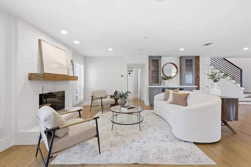 4310 Forest Bend Road, Dallas, TX 75244 Spacious living area featuring light wood-finish flooring, a white brick fireplace with a wood mantel, recessed lighting, and white plantation shutters