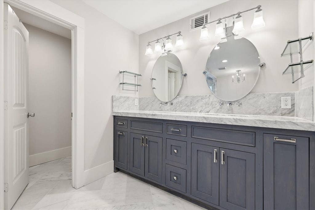4310 Forest Bend Road, Dallas, TX 75244 Double vanity with dark wood cabinetry, light stone countertop, oval mirrors, and wall-mounted lighting fixtures