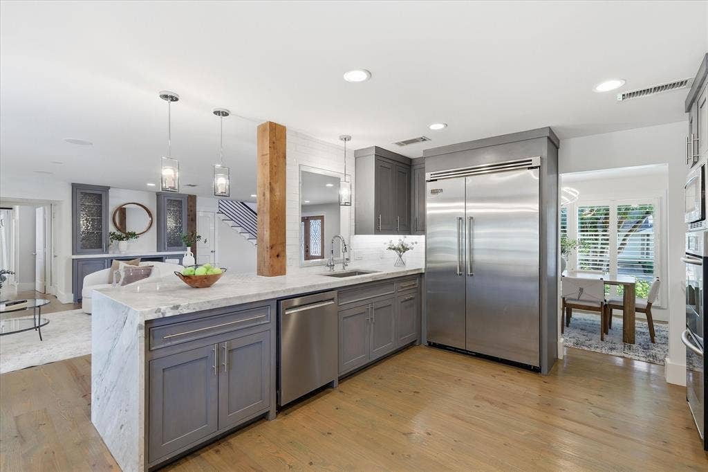 4310 Forest Bend Road, Dallas, TX 75244 Open concept kitchen featuring an oversized island with gray shaker cabinetry, stainless steel appliances, pendant lighting, and wood-finish flooring