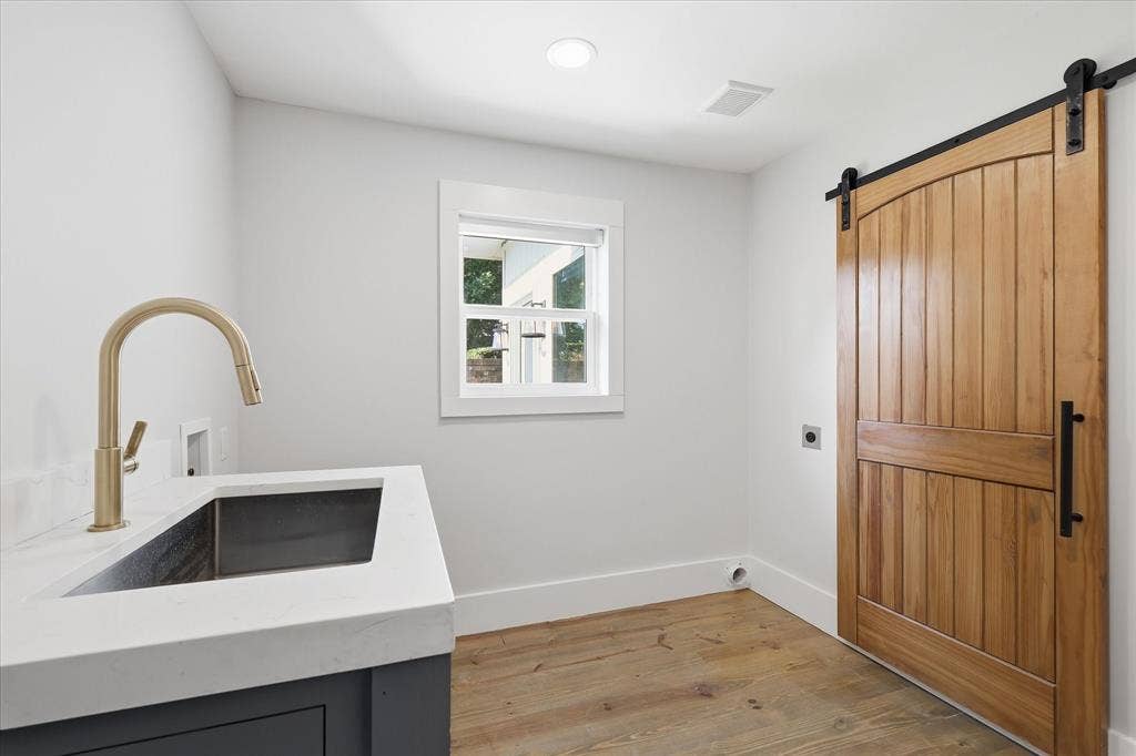4310 Forest Bend Road, Dallas, TX 75244 Laundry area featuring a wood-finish barn door, light wood-finish flooring, and a window with white trim