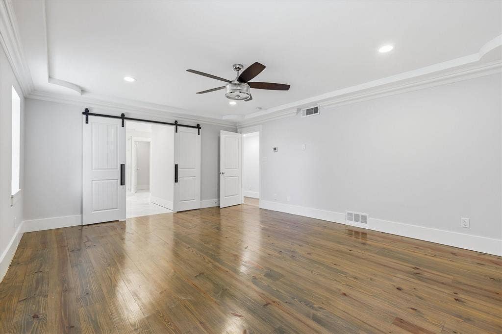 4310 Forest Bend Road, Dallas, TX 75244 Spacious room featuring wide plank wood-finish flooring, white barn doors with black hardware, crown molding, and recessed lighting