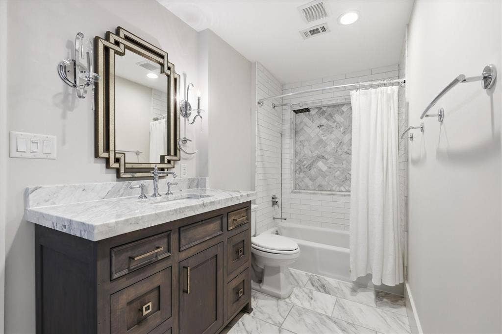 4310 Forest Bend Road, Dallas, TX 75244 Bathroom featuring a wood vanity with a white countertop and undermount sink, geometric mirror, and sconce lighting